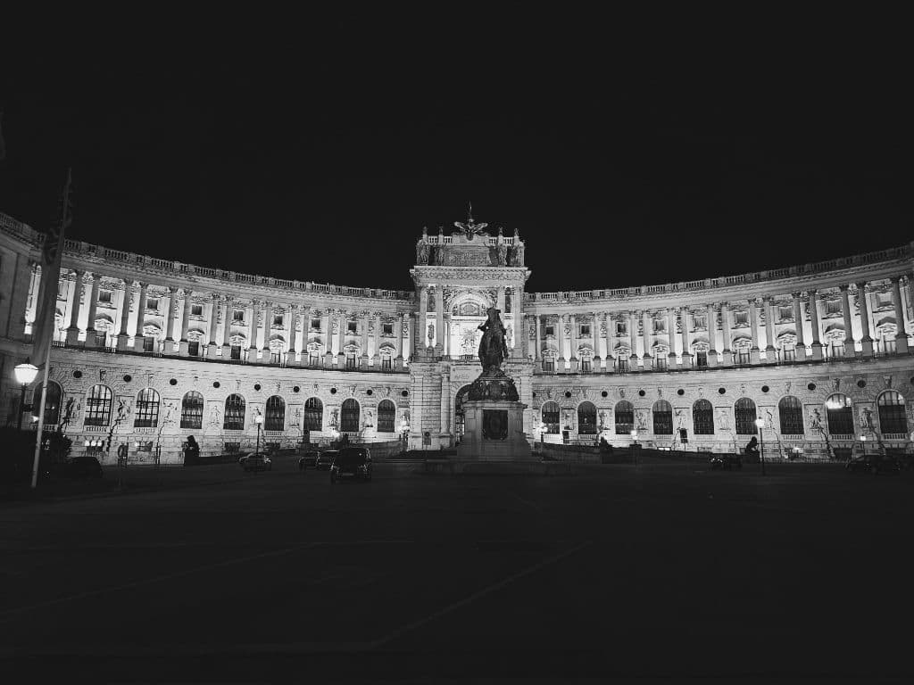 Siyah-beyaz kare: Neue Burg Hofburg Sarayı'nın gece aydınlatılmış kavisli cephesi ve atlı heykel.